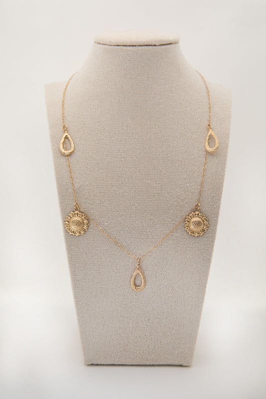 Gold necklace with sunflower and teardrop pendants on a gray mannequin bust against a white background