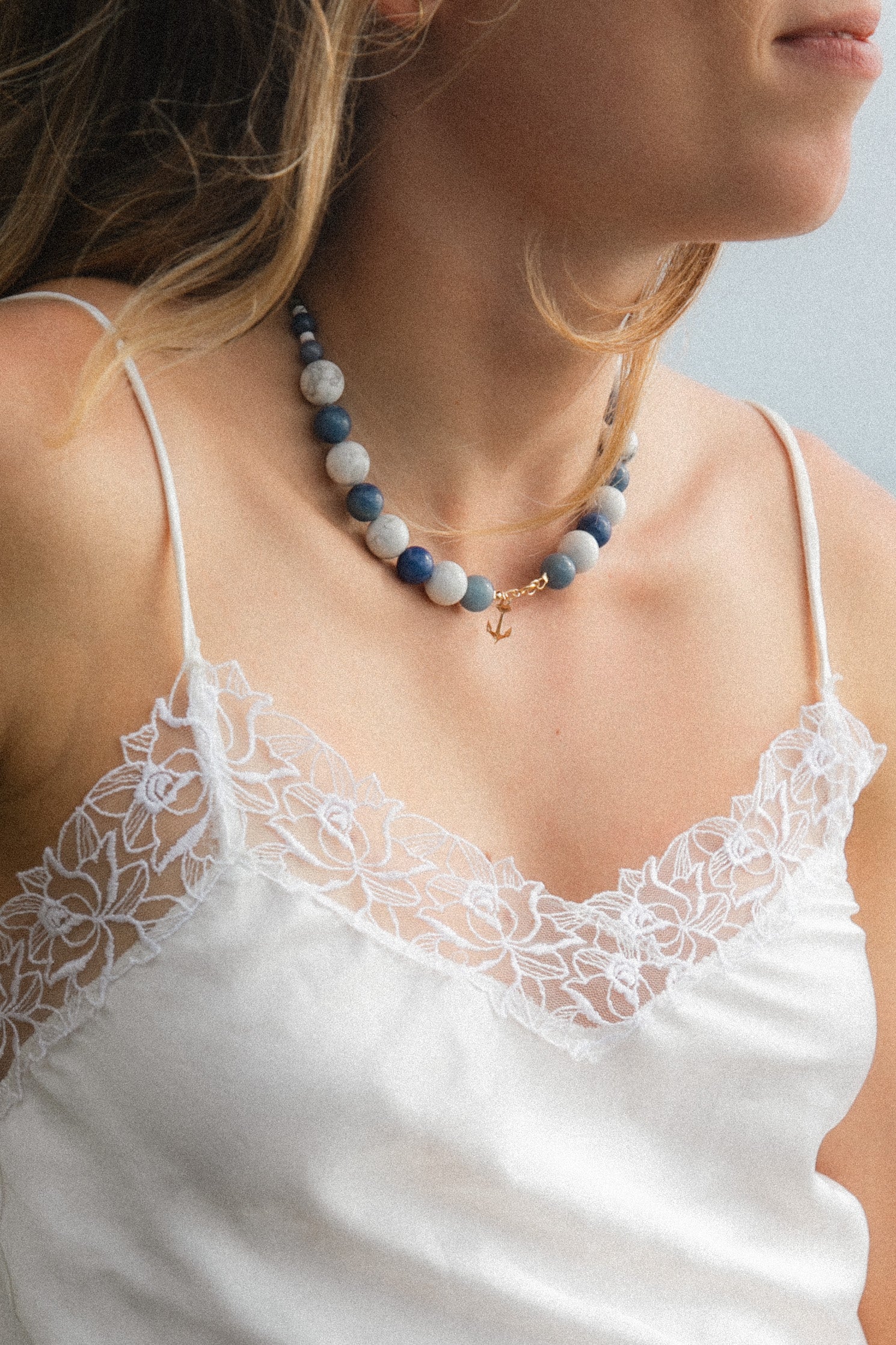 A girl wearing a blue and white handmade necklace made of semi-precious stones and gold-filled anchor charm. 