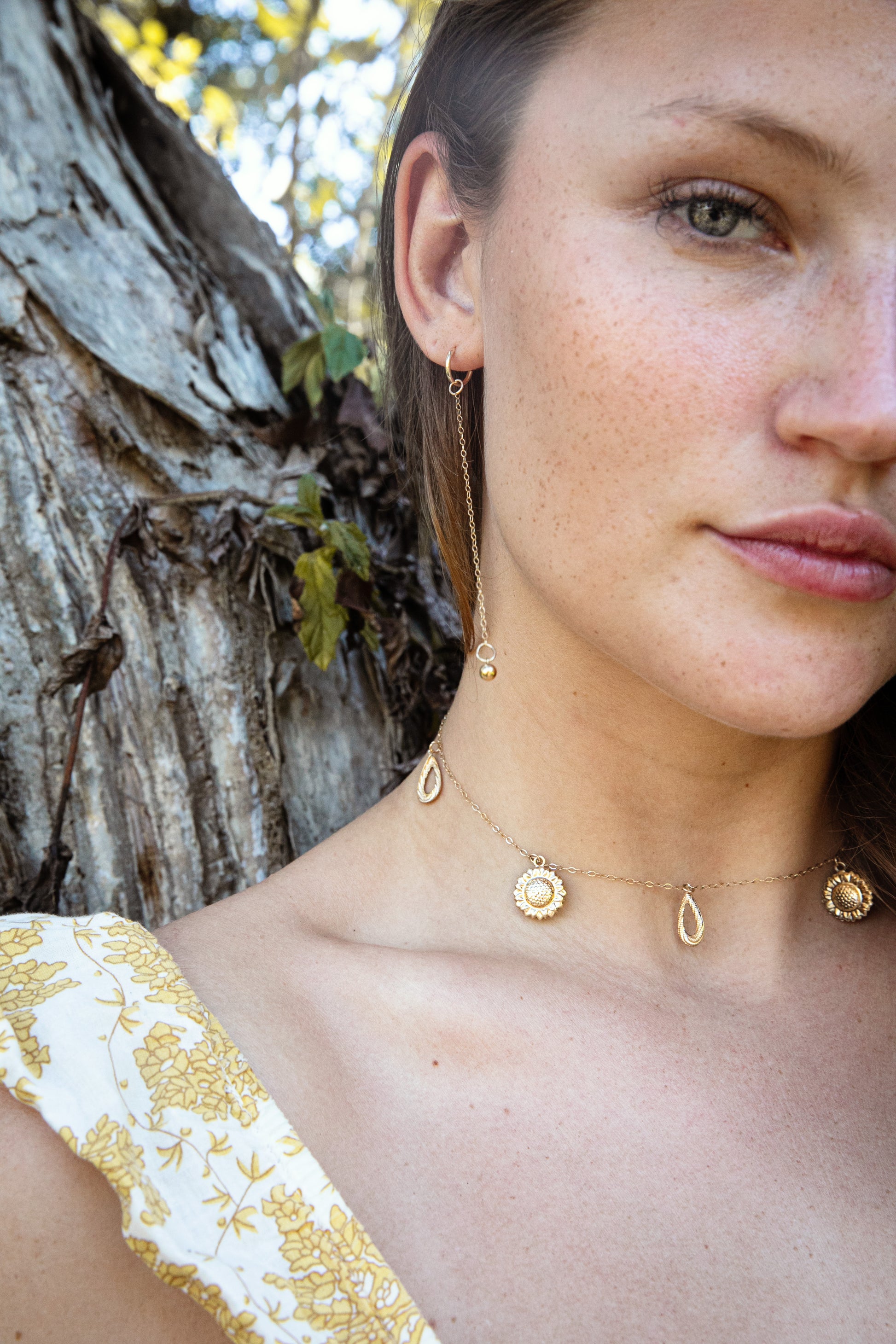 Woman wearing gold necklace with a sunflower charms and tear drops in the south of France. 
