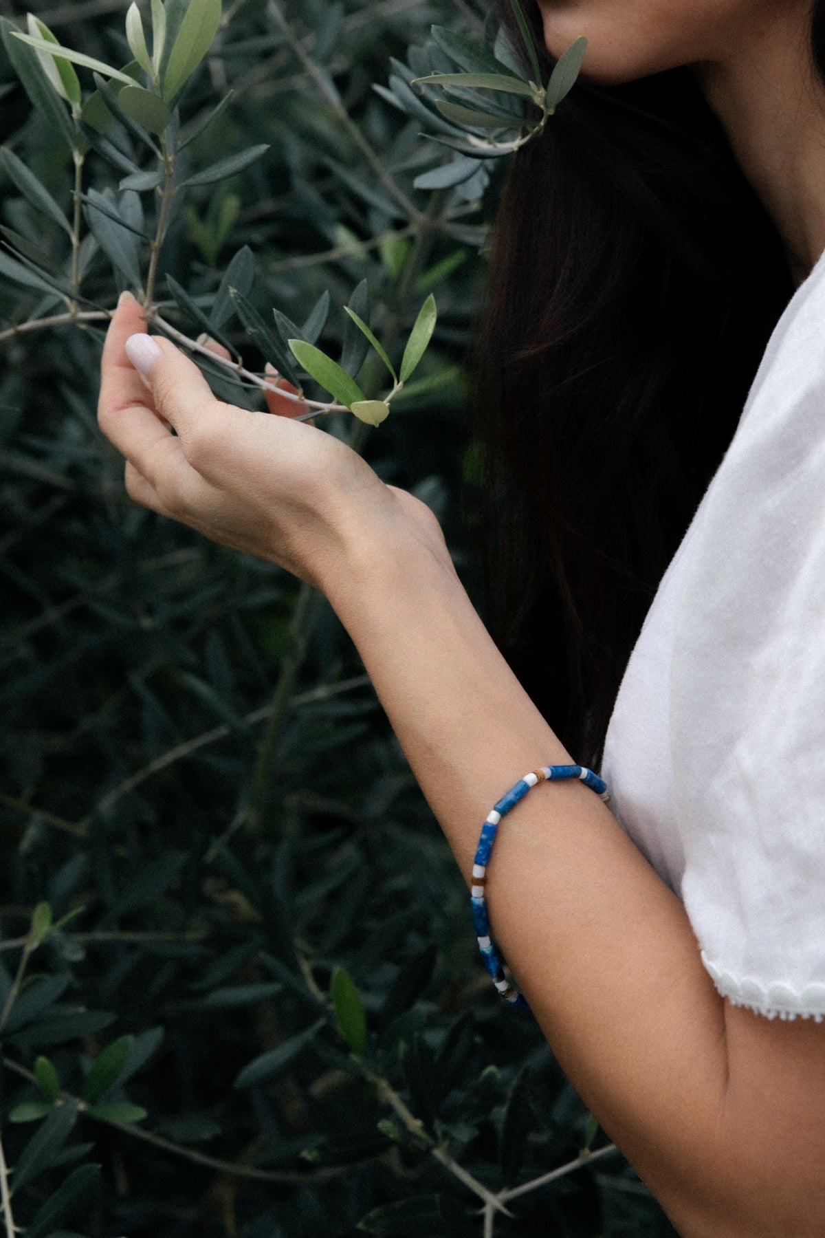 Person holding an olive branch and wearing a handcrafted bracelet made of lapis lazuli and red carnelian semi-precious stones. 