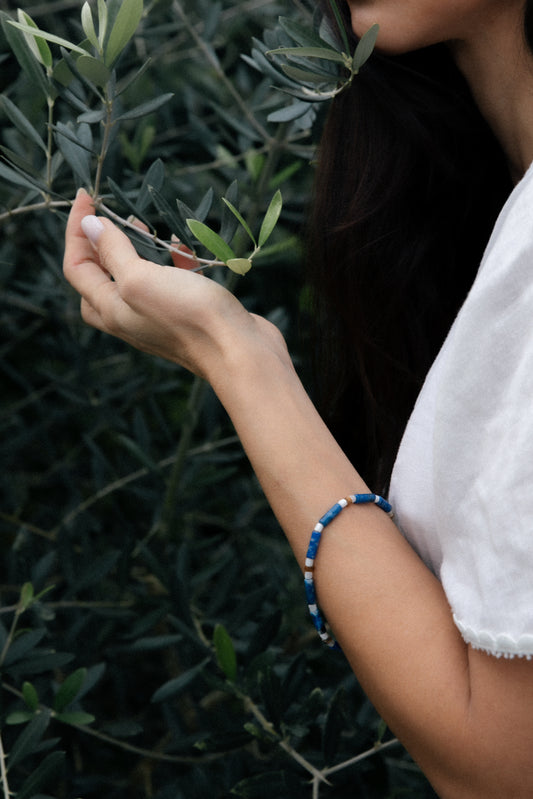 Person holding an olive branch and wearing a handcrafted bracelet made of lapis lazuli and red carnelian semi-precious stones. 